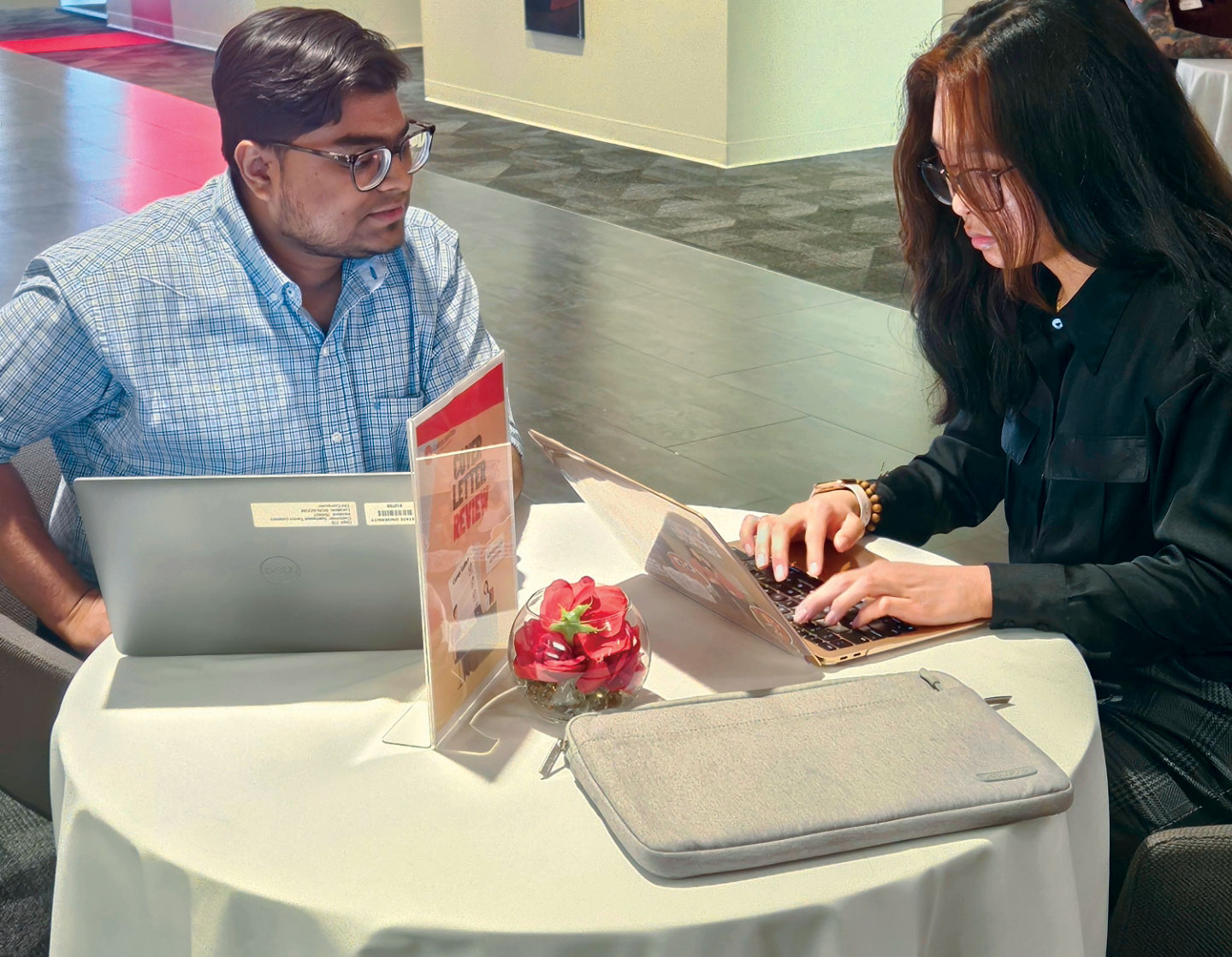 student and staff sitting together at table with laptops