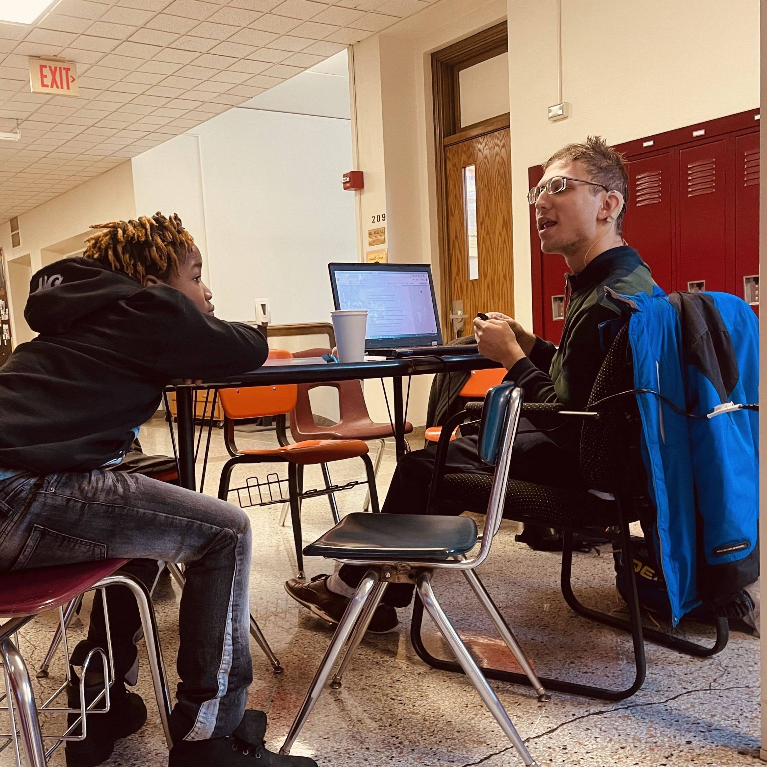 Undergraduate talking with a student at their desks.