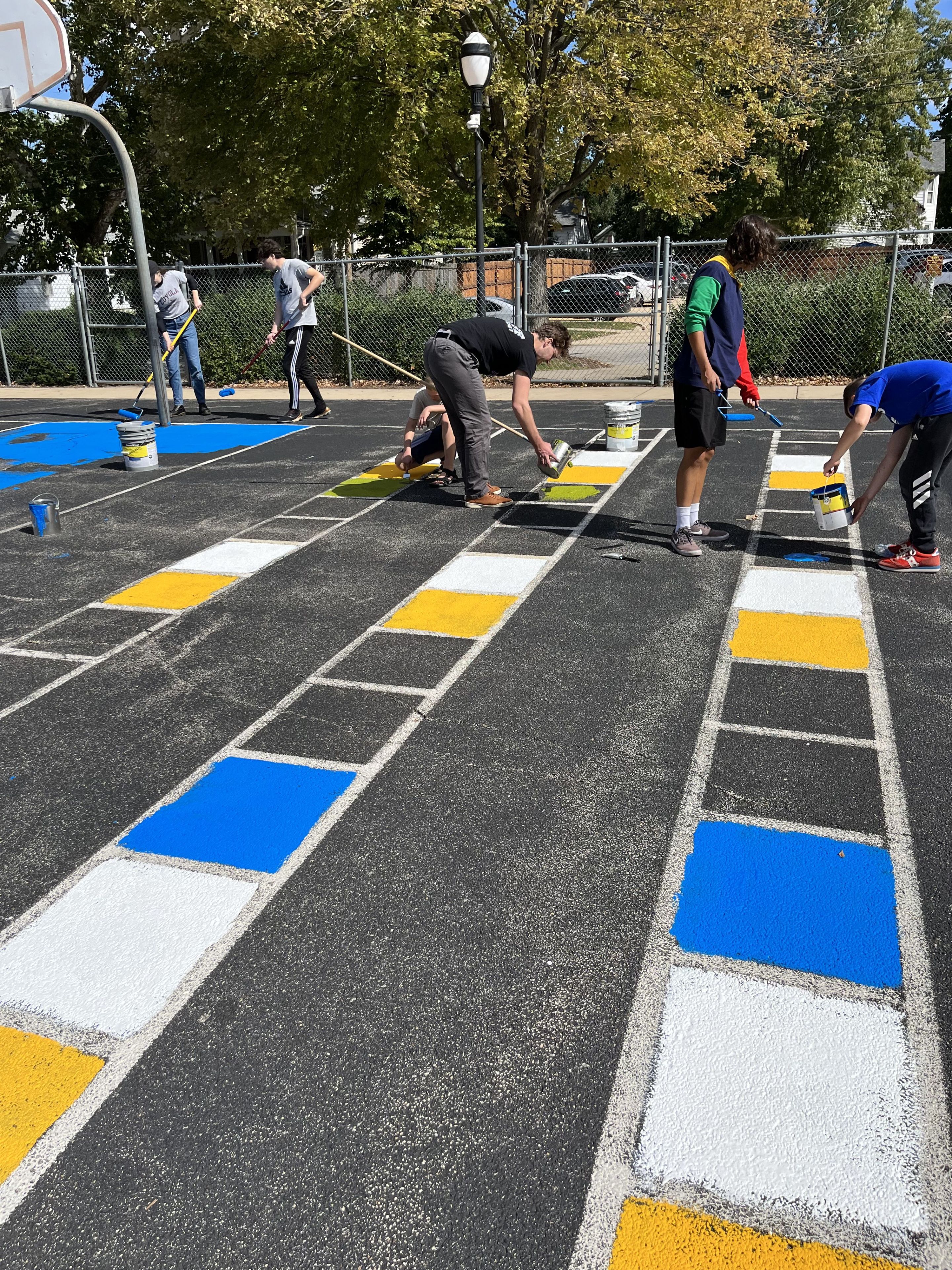 Five individuals filling in squares with paint on the school's asphalt.