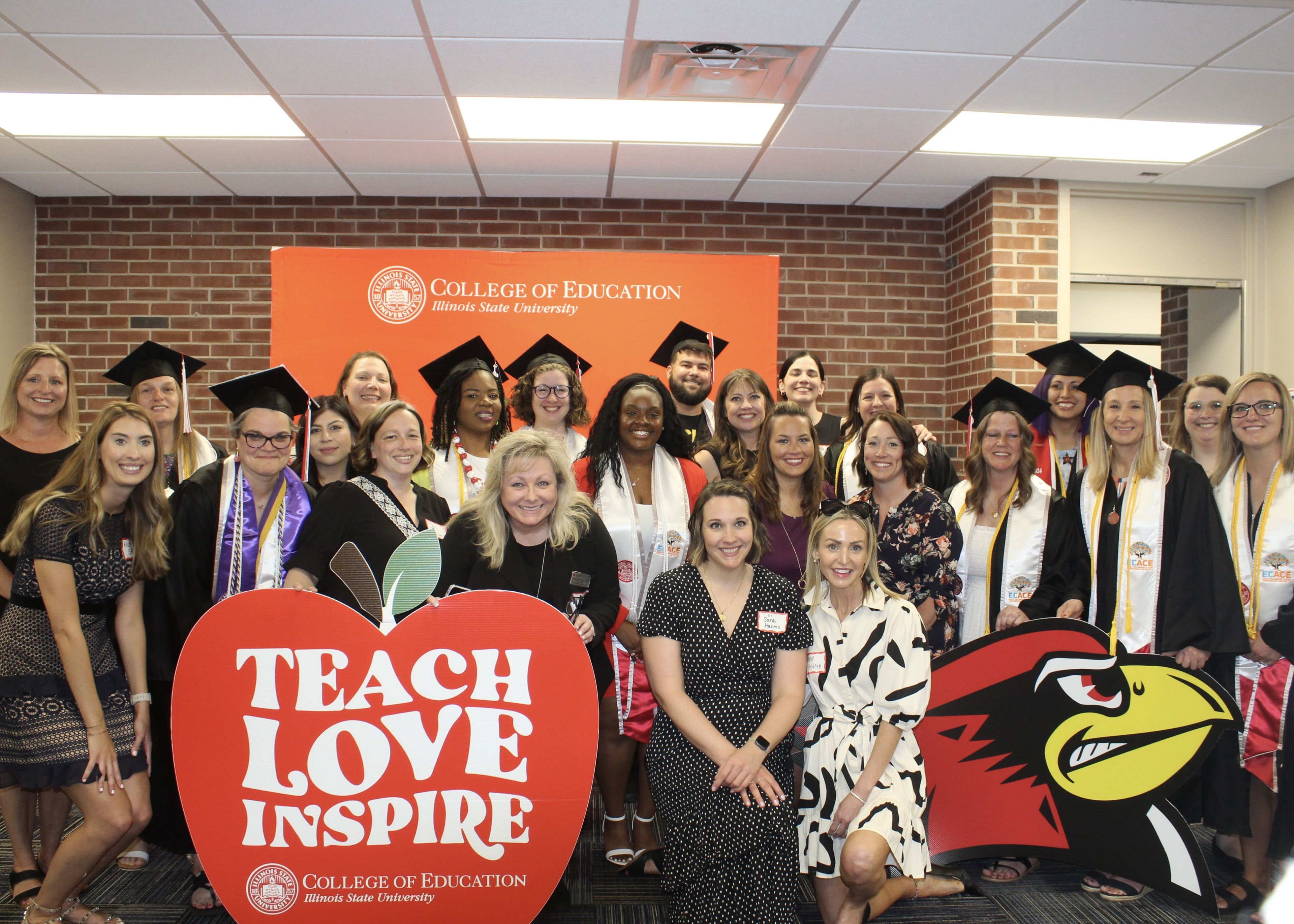 People standing for group photo behind an apple shaped sign reading "Teach Love Inspire"
