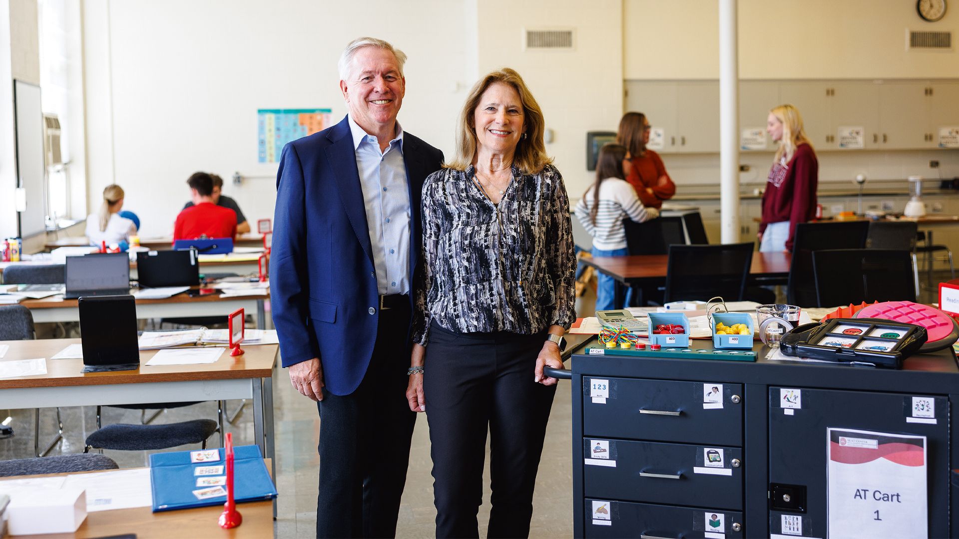 Steve and Sharon Hagge standing next to a cart loaded with a variety of assistive technology devices.
