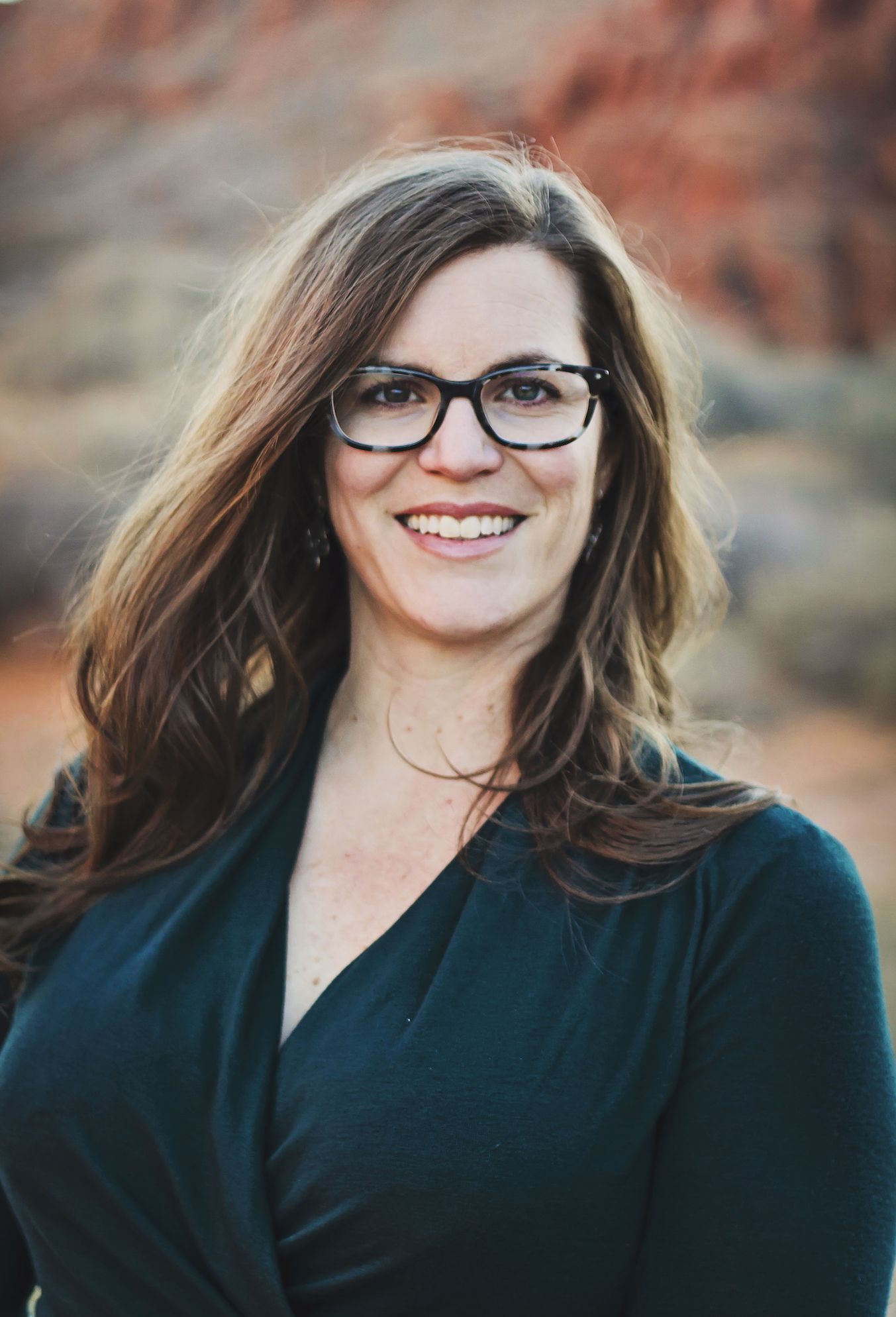 Dr. Anna Smith, smiling with long brown hair and glasses, wearing a black top outdoors.